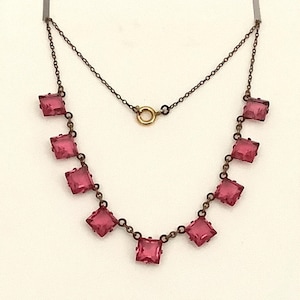 May include: A vintage necklace with square, pink gemstones set in a dark metal chain. The necklace has a delicate design with a small clasp and is displayed against a white background. The gemstones are evenly spaced.