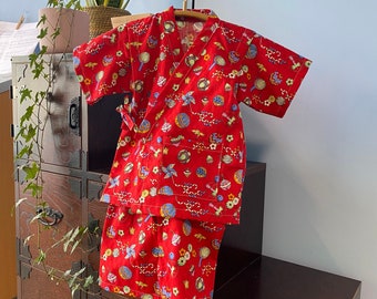 May include: Red and white patterned kimono-style top and matching pants for a child. The fabric features a whimsical design of small toys and flowers.