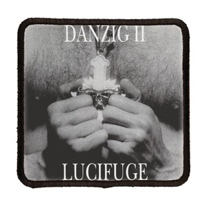 May include: Black and white photo of a person holding a silver cross with a skull on it. The text "DANZIG II LUCIFUGE" is printed on the image.
