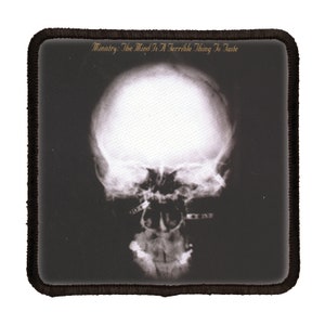 May include: Black and white image of a skull with metal bars across the mouth. The text "Ministry: The Mind Is A Terrible Thing To Taste" is at the top of the image.