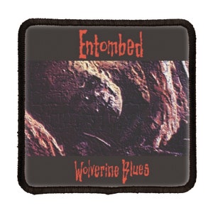 May include: A black and white patch with the band name "Entombed" in red text and the album title "Wolverine Blues" in red text.