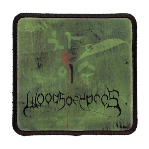 Puede incluir: Un parche bordado verde y negro con el nombre de la banda "Woods of Yore" en una fuente estilizada. El parche tiene un diseño de salpicaduras rojas en el fondo.