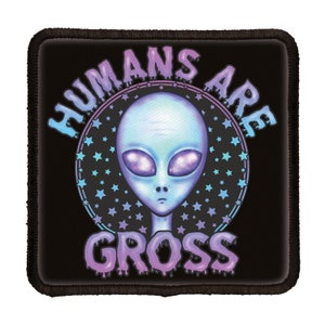 May include: A black patch with a white outline features a blue alien with purple eyes and a dripping text graphic that reads "HUMANS ARE GROSS" in a purple and pink font.