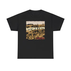 May include: Black t-shirt with a graphic design. The design features the text "SYSTEM OF A DOWN" in white above the word "Toxicity" in red. The design depicts a landscape in brown and gold tones.