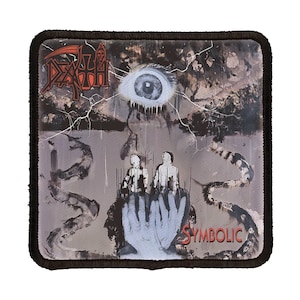 May include: A black and white patch with a band logo and the word "Symbolic". The logo is a stylized skull with a large eye in the background.