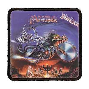 May include: A purple and black embroidered patch with a metal winged creature riding a motorcycle with a large saw blade. The text "Painkiller" and "Judas Priest" are visible on the patch.