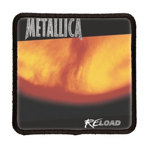 May include: A black and white square patch with the band name "Metallica" in white text at the top and the album title "Reload" in white text at the bottom. The background is a blurry image of a fiery orange and yellow colour.