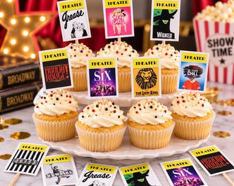 May include: A collection of vanilla cupcakes with white frosting and multi-colored sprinkles, each topped with a rectangular paper topper featuring various Broadway musical titles like Grease, Mean Girls, Wicked, Moulin Rouge, Six, and The Lion King.