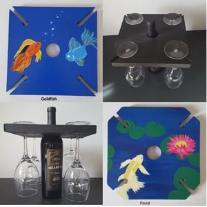 Puede incluir: Cuatro diseños diferentes de portavasos para vino. El primer diseño es azul con un pez dorado y un pez azul. El segundo diseño es negro con seis portavasos. El tercer diseño es negro con tres portavasos y una botella de vino. El cuarto diseño es azul con una escena de estanque y un pez blanco.