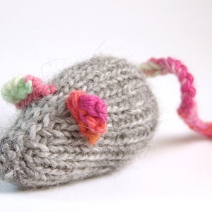 Könnte beinhalten: Ein graues, gestricktes Mauspüppchen mit rosa, grünen und orangen Garn-Akzenten. Die Maus hat einen langen Schwanz.