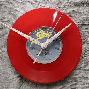May include: A red vinyl record clock featuring a white clock face with black hands. The record label is for Michael Jackson's "Don't Stop 'Til You Get Enough" song, released on Epic Records.