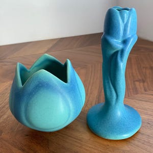 May include: A matte turquoise ceramic bowl with a scalloped petal-like rim and a matching tall ceramic candlestick holder shaped like a closed tulip flower, both featuring a smooth finish and a gradient of blue and green tones.