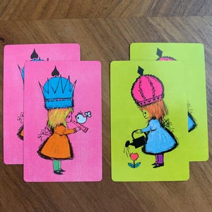May include: Four rectangular playing cards featuring stylized illustrations. Two pink cards show a figure in an orange dress and blue crown with a bird. Two lime green cards show a figure in a blue dress and pink crown watering a heart-shaped flower.