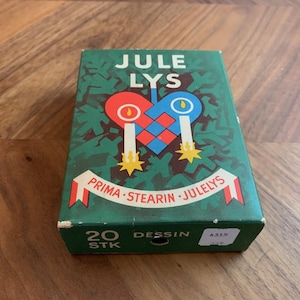 Pu&ograve; includere: Una scatola verde con le parole "JULE LYS" in bianco, con un disegno a forma di cuore con candele e la scritta "PRIMA STEARIN JULELYS". La scatola ha anche la scritta "20 STK" e "DESSIN".
