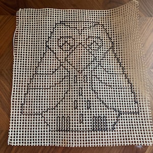 May include: A beige canvas with a black outline of a cartoon character. The character is a person with a large head and a long beard. The character is wearing a long robe.