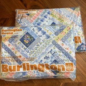 Op de afbeelding: Twee verpakkingen Burlington House eenpersoonslakens in doorzichtig plastic. De stof heeft een blauw, wit en geel patchwork bloemenpatroon met strepen en stippen. De verpakking toont de merknaam Burlington House in oranje letters.