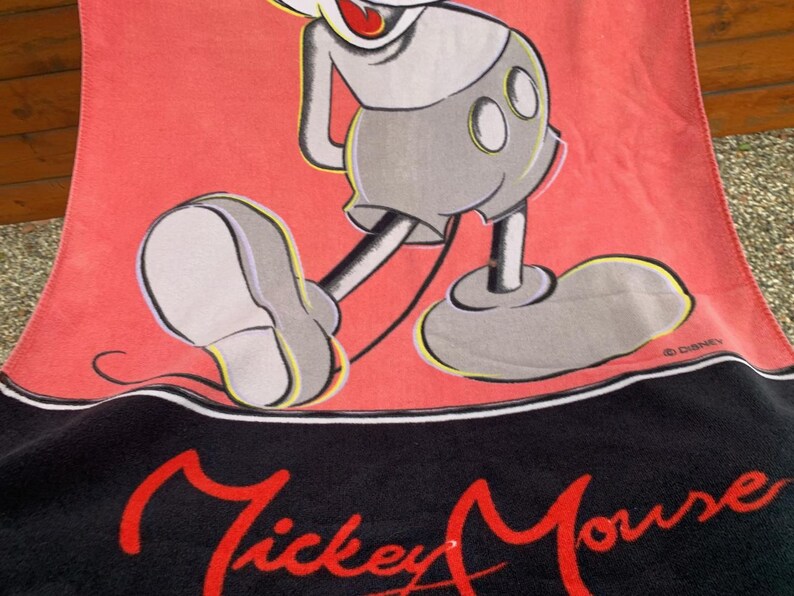 Może przedstawiać: Czerwony i czarny ręcznik Mickey Mouse z dużą ilustracją Myszki Miki. Ręcznik ma napis "Mickey Mouse" w czerwonym skrypcie na dole, klasyczny design Disneya.