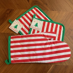 May include: Red and white striped oven mitt and pot holders with green trim. The oven mitt is quilted and has a loop for hanging. The pot holders are square and rectangular. Each item has a tag with a Christmas tree and the word "Marimekko".