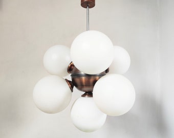 May include: A modern, mid-century style chandelier with a copper finish and six white globe-shaped glass shades.