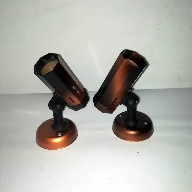 May include: Two brown and black metal spotlights with a copper base. The spotlights are angled towards the right and left.
