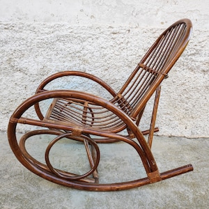 Puede incluir: Una mecedora de mimbre marr&oacute;n con respaldo curvo y asiento redondeado. La silla est&aacute; hecha de materiales naturales y tiene un aspecto r&uacute;stico.