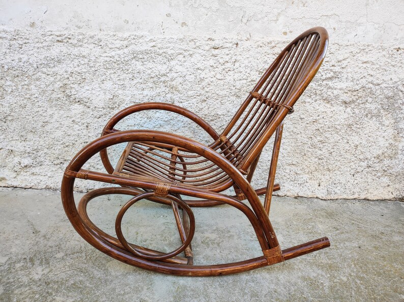 Puede incluir: Una mecedora de mimbre marr&oacute;n con respaldo curvo y asiento redondeado. La silla est&aacute; hecha de materiales naturales y tiene un aspecto r&uacute;stico.