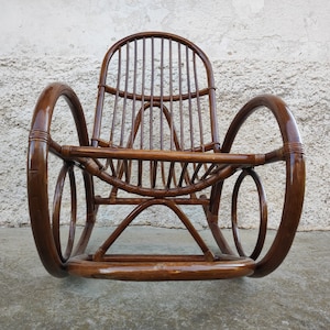 Puede incluir: Una mecedora de mimbre marr&oacute;n con respaldo y brazos curvos. La silla est&aacute; hecha de rat&aacute;n natural tejido y tiene un acabado liso y pulido.