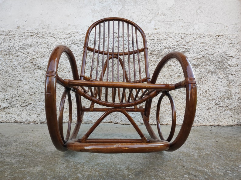 Puede incluir: Una mecedora de mimbre marr&oacute;n con respaldo y brazos curvos. La silla est&aacute; hecha de rat&aacute;n natural tejido y tiene un acabado liso y pulido.