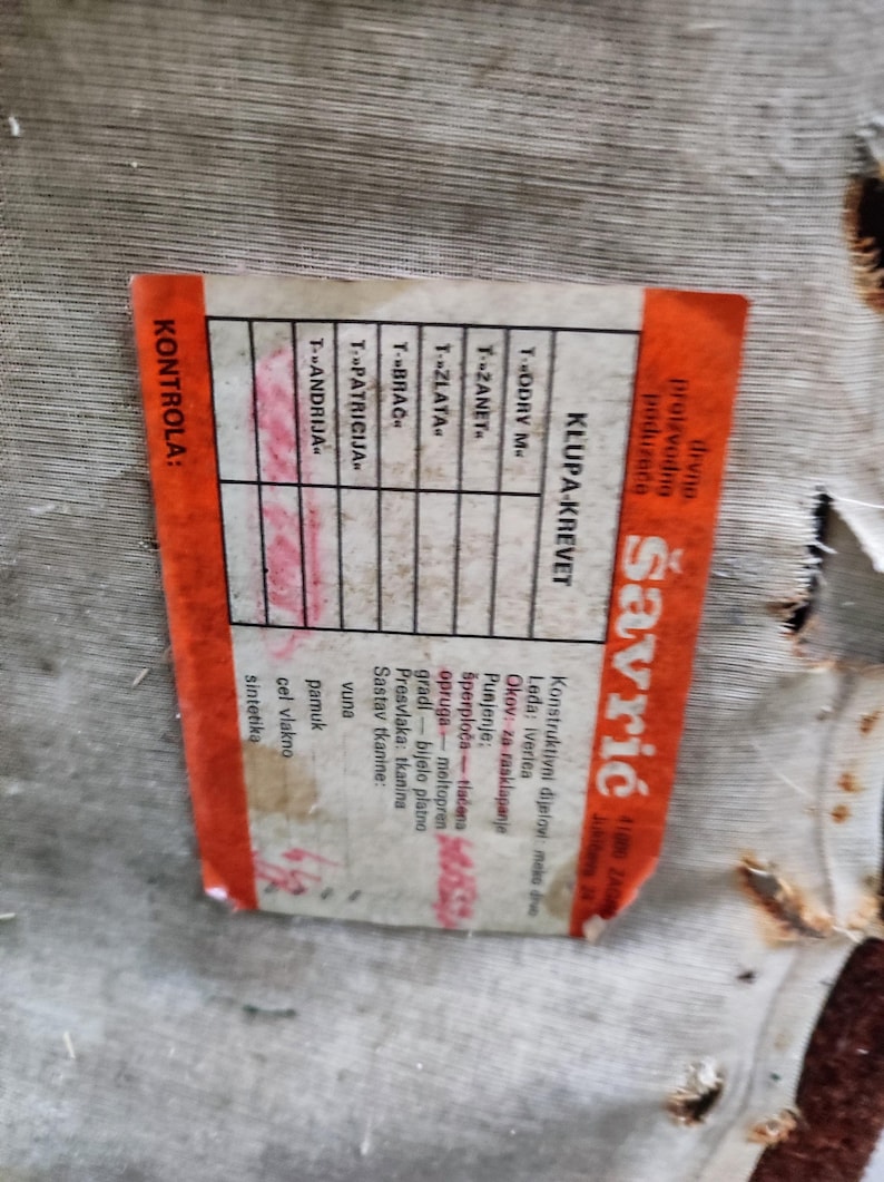 May include: A close-up of a red and orange label with the text "KLUPA-KREVET" and "Savrić" in white. The label also includes a table with the headings "T-ODRV M", "T-ZANET", "TZLATA", "T-BRAC", "T-PATRICIJA", "T-ANDRIJA" and a column with the headings "Konstruktivni dijelovi", "Leda", "Okov", "Punjenje", "Presvlaka", "Sastav tkanine".