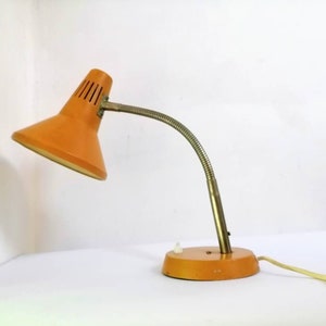 May include: A vintage orange desk lamp with a flexible arm and a round base. The lamp has a white interior and a metal shade with small holes.