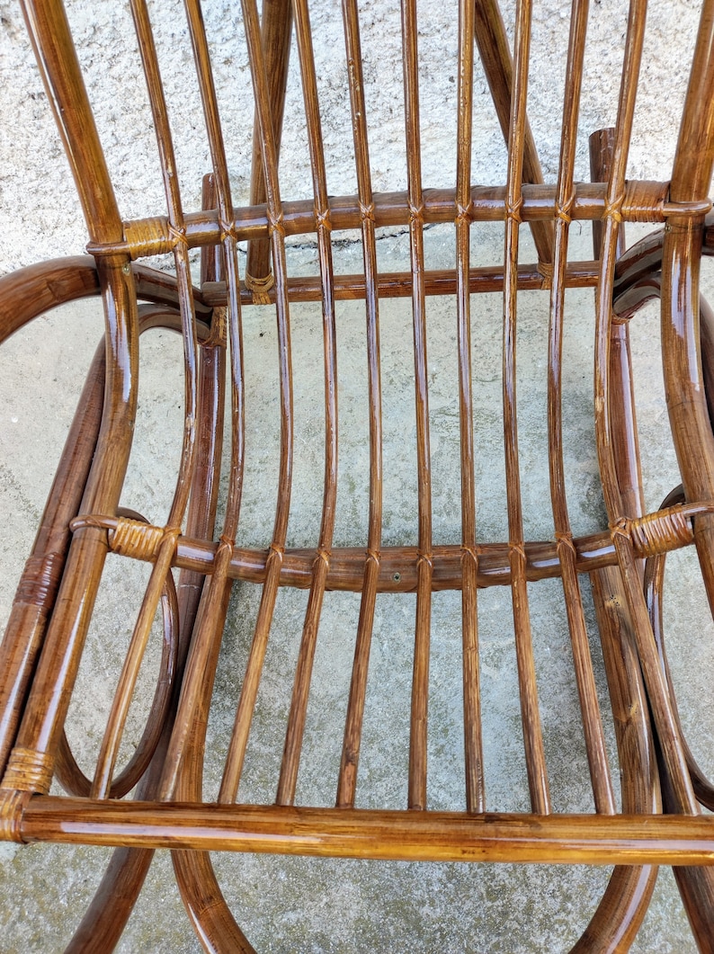 Puede incluir: Primer plano de una mecedora de mimbre marr&oacute;n con acabado brillante. La silla est&aacute; hecha de mimbre tejido y tiene un respaldo y un asiento curvos.
