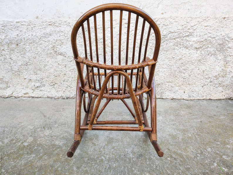 Puede incluir: Una mecedora de mimbre marr&oacute;n con respaldo curvo y asiento tejido. La silla est&aacute; hecha de materiales naturales y tiene un aspecto r&uacute;stico.
