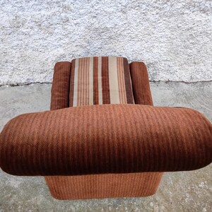 May include: A brown striped armchair with a brown and white striped cushion. The chair has a high back and wide arms.