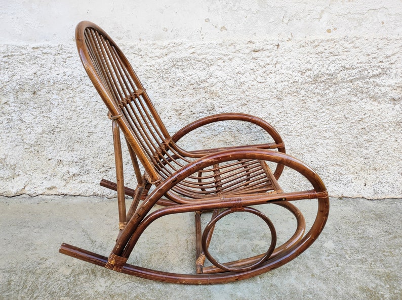 Puede incluir: Una mecedora de mimbre marr&oacute;n con respaldo curvo y asiento redondeado. La silla est&aacute; hecha de rat&aacute;n tejido natural y tiene un aspecto r&uacute;stico y vintage.