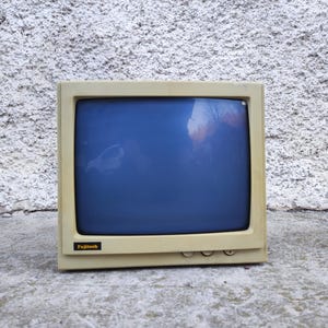 以下が含まれることがあります： 青い画面のオフホワイトのヴィンテージFujitechコンピューターモニター。モニターは角が丸い長方形で、小さなFujitechのロゴが付いています。下部には3つのボタンがあります。