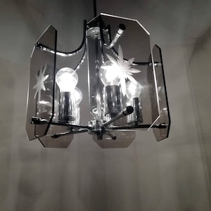 May include: A vintage chandelier with a chrome finish and clear glass panels. The panels are etched with starburst designs. The light fixture has four exposed light bulbs. The overall design is mid-century modern.