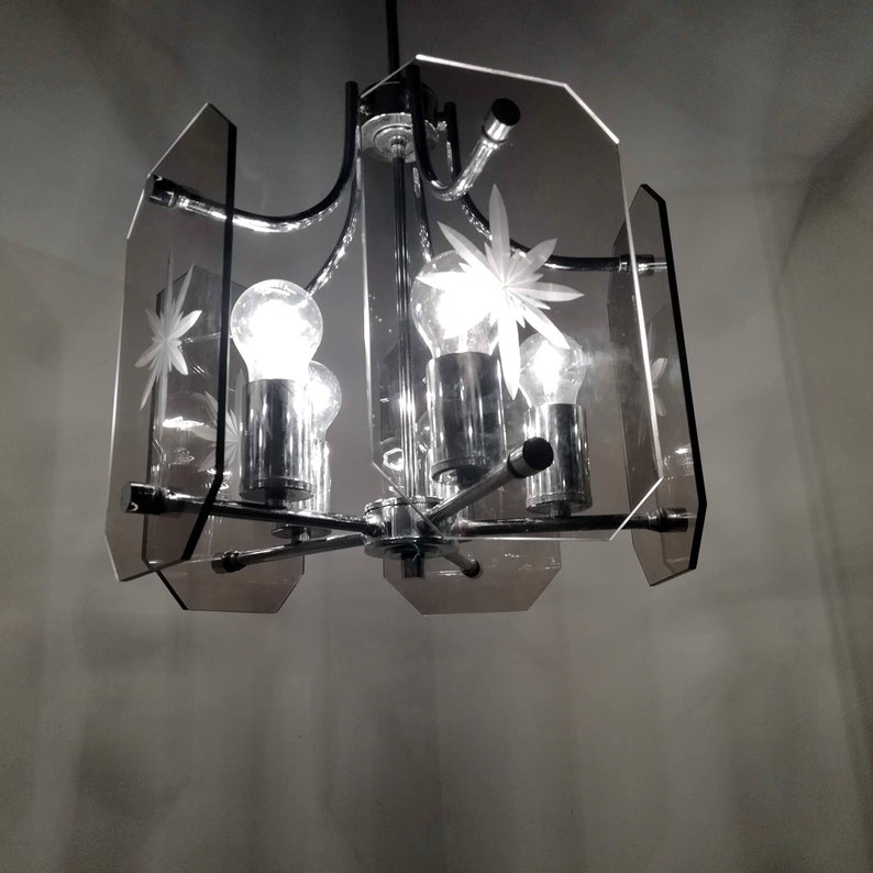 May include: A vintage chandelier with a chrome finish and clear glass panels. The panels are etched with starburst designs. The light fixture has four exposed light bulbs. The overall design is mid-century modern.