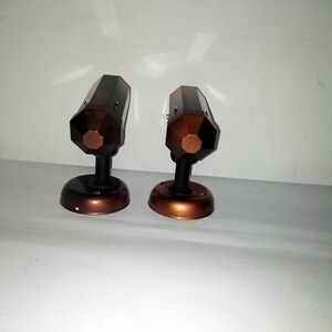 May include: Two brown and black metal wall sconces with a geometric design. The sconces have a round base and a pointed top.