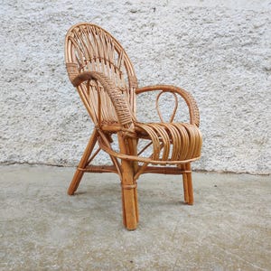May include: A vintage rattan chair with a high back and armrests. The chair is made from woven natural rattan, in a light brown colour. The design features a curved back and seat, with a sturdy base.