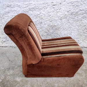 May include: A brown corduroy armchair with a striped pattern in shades of brown, beige, and white. The chair has a high back and a curved seat.