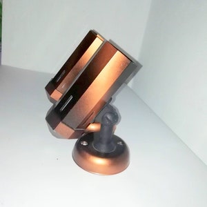 May include: A copper-colored security camera with a black base and a swivel mount. The camera has two lenses and is mounted on a wall.