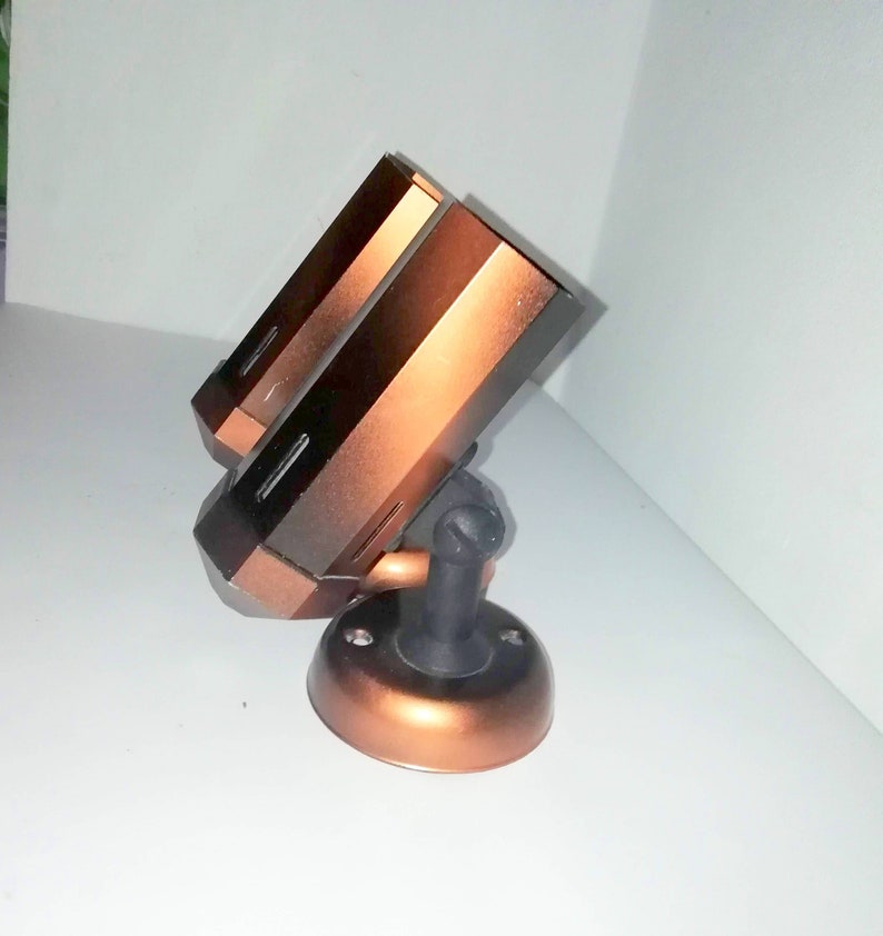 May include: A copper-colored security camera with a black base and a swivel mount. The camera has two lenses and is mounted on a wall.