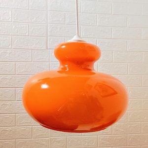 Könnte beinhalten: Eine leuchtend orangefarbene Glaspendelleuchte mit runder, bauchiger Form. Die Leuchte hängt an einer weißen Decke.