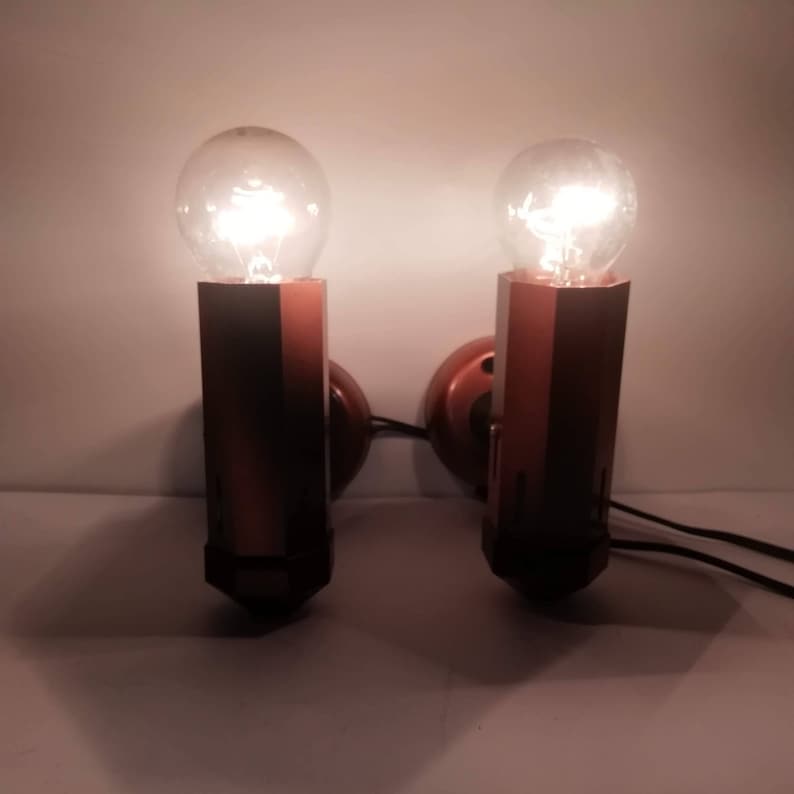 May include: A pair of wall-mounted light fixtures with brown metal bases and clear glass bulbs. The bulbs are lit and casting a warm glow.