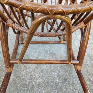 Puede incluir: Una mecedora de mimbre marr&oacute;n con asiento y respaldo tejidos. La silla est&aacute; hecha de materiales naturales y tiene un aspecto r&uacute;stico.