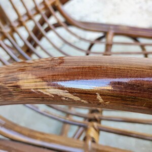 Puede incluir: Primer plano de una mecedora de mimbre marr&oacute;n con un acabado brillante. La silla tiene un dise&ntilde;o tejido y muestra signos de desgaste.