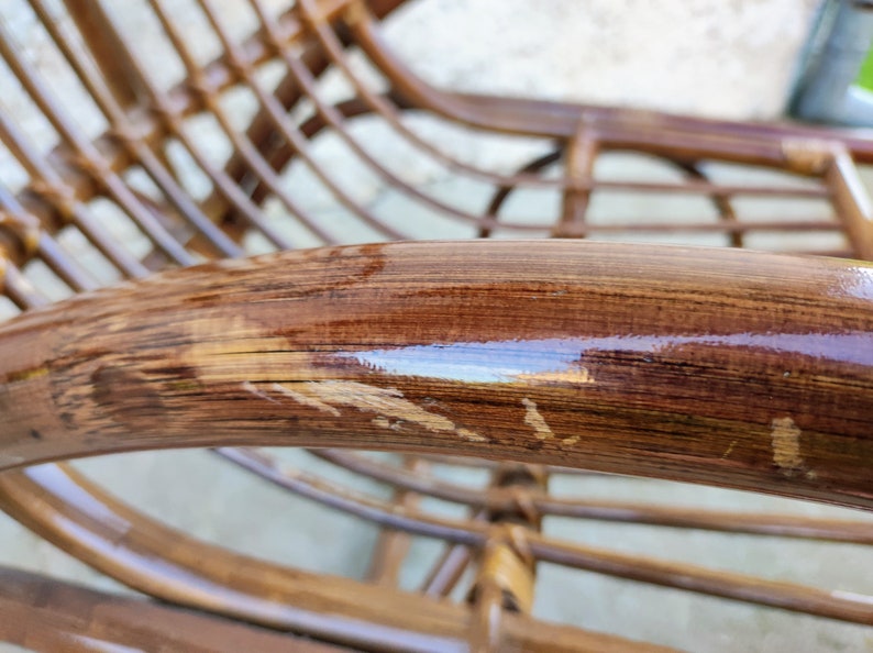 Puede incluir: Primer plano de una mecedora de mimbre marr&oacute;n con un acabado brillante. La silla tiene un dise&ntilde;o tejido y muestra signos de desgaste.