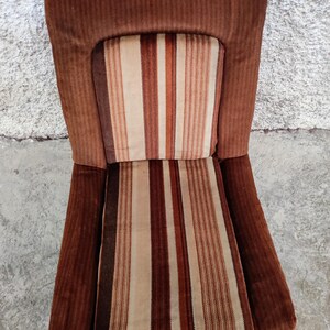 May include: A brown striped armchair with a high back and a brown corduroy fabric. The chair has a striped cushion with brown, white, and orange stripes.