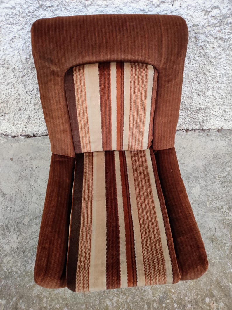 May include: A brown striped armchair with a high back and a brown corduroy fabric. The chair has a striped cushion with brown, white, and orange stripes.