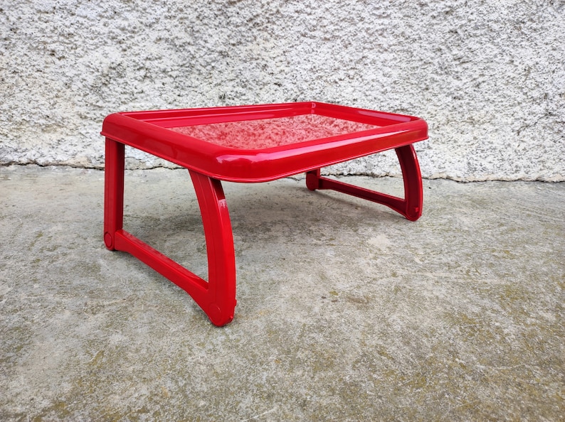 K&ouml;nnte beinhalten: Ein leuchtend roter, kleiner, tragbarer Laptop-Tisch mit rechteckiger Oberseite und geschwungenen Beinen. Der Tisch ist aus Kunststoff gefertigt und f&uuml;r die Nutzung auf einem Bett oder Sofa konzipiert. Er misst ca. 46 cm lang, 30 cm breit und 20 cm hoch.